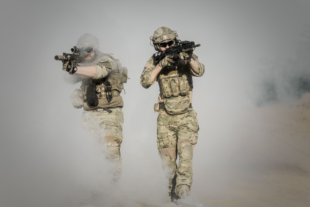 Two soldiers advancing through dust in full combat gear